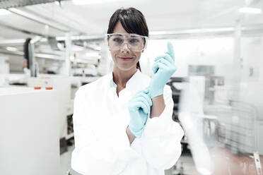 Smiling mature female scientist wearing gloves at laboratory - JOSEF02300