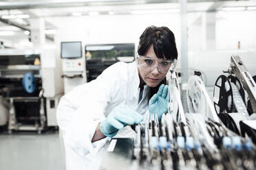 Mature female technician examining machinery in bright industry - JOSEF02304