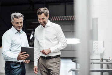 Smiling businessmen discussing over digital tablet while standing in industry - JOSEF02310