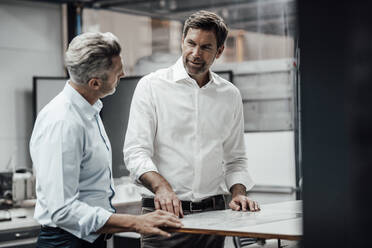 Smiling mature businessman discussing while standing with male colleague in factory - JOSEF02313