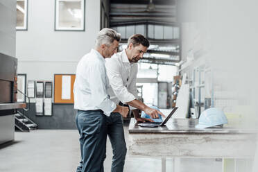 Männliche Ingenieure diskutieren am Laptop an einem Tisch in der Industrie - JOSEF02320