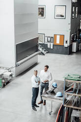 Male colleagues standing by table in manufacturing industry - JOSEF02323