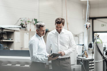 Mature male engineers discussing over digital tablet while standing in manufacturing industry - JOSEF02329