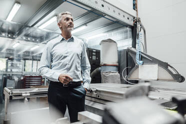 Male engineer looking away while standing by manufacturing equipment in factory - JOSEF02336