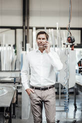 Male engineer looking away while talking on smart phone in factory - JOSEF02347