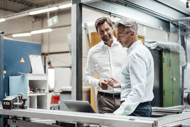 Männliche Ingenieure diskutieren in einer Fabrik über einem Laptop - JOSEF02354