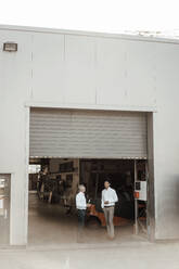 Reife Geschäftsleute, die am Eingang einer Fabrik stehen und diskutieren - JOSEF02357
