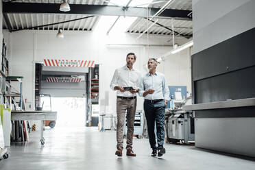 Männliche Ingenieure schauen beim Gehen in der Fabrik weg - JOSEF02363