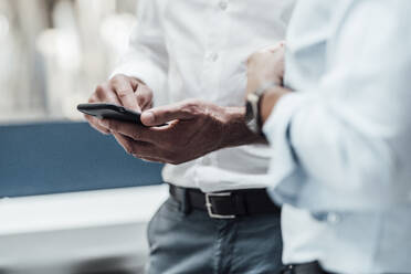 Businessman using smart phone while standing by male colleague in industry - JOSEF02378