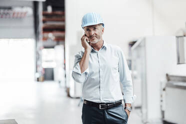 Male engineer looking away while talking on mobile phone in factory - JOSEF02389