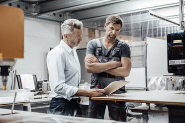 Älterer Manager, der mit einem Arbeiter über ein Dokument diskutiert, während er in einer Fabrik steht - JOSEF02415