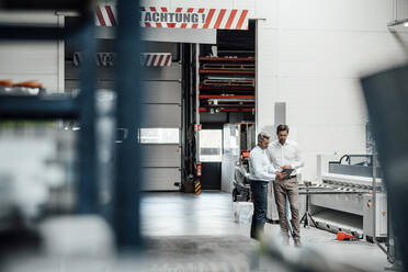 Male engineers discussing over digital tablet while standing in factory - JOSEF02426