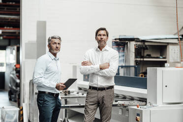 Male engineers looking away while standing by machinery in factory - JOSEF02428