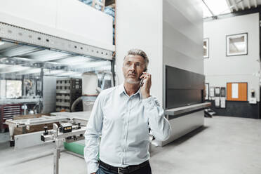 Male engineer looking away while talking on smart phone in factory - JOSEF02432