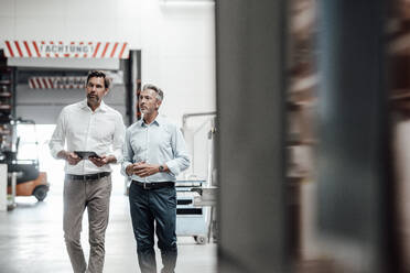 Mature male engineers discussing while walking in factory - JOSEF02443