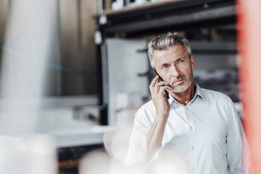 Contemplating engineer looking away while talking on smart phone in factory - JOSEF02461