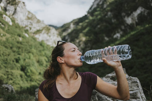 Mittlere erwachsene Wanderin, die aus einer Plastikwasserflasche trinkt und dabei wegschaut - DMGF00274