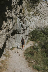 Woman hiking on trail by rocky cliff during sunny day - DMGF00282