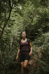 Woman hiking amidst green plants in forest - DMGF00287