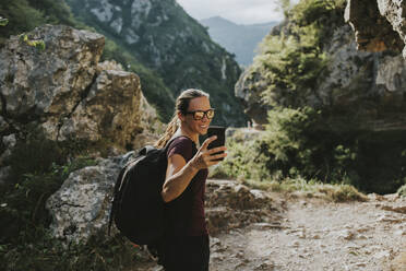 Lächelnde Trekkerin, die beim Wandern ein Selfie mit ihrem Smartphone macht - DMGF00290