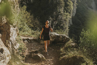 Female trekker hiking downhill on trail during sunny day - DMGF00293