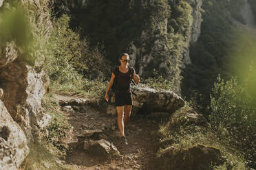 Weibliche Wanderin, die an einem sonnigen Tag auf einem Pfad bergab wandert - DMGF00293