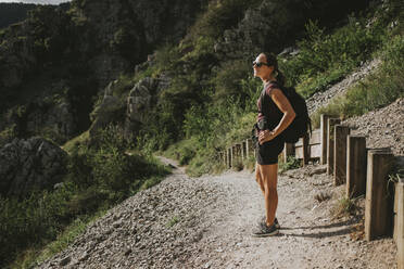 Woman with backpack admiring nature while taking break during hiking - DMGF00294