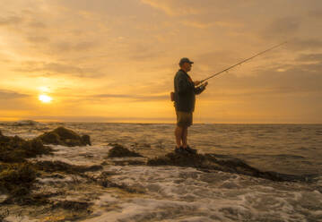 Maine coastal fisherman waits for a striped bass to bite as sun rises. - CAVF90219