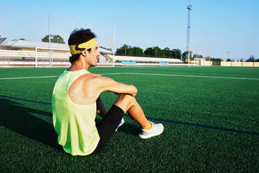 Young guy in sportswear looks at the horizon sitting on the grass - CAVF90243