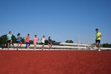 Gruppe von Frauen übt mit ihrem jungen Trainer vor dem Training Stretching - CAVF90250