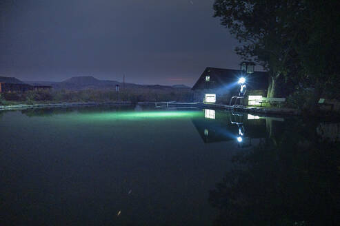 Person, die nachts mit eingeschalteter Stirnlampe neben einem Schwimmbecken steht - CAVF90277