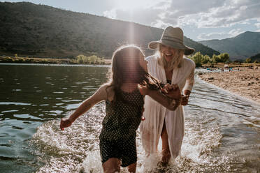 Happy mom chasing young daughter through water - CAVF90279