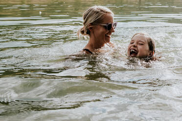 Mutter und kleine Tochter schwimmen an einem sonnigen Tag freudig in einem See - CAVF90286