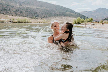 Porträt einer glücklichen Mutter und Tochter beim Spielen in einem See an einem sonnigen Tag - CAVF90287