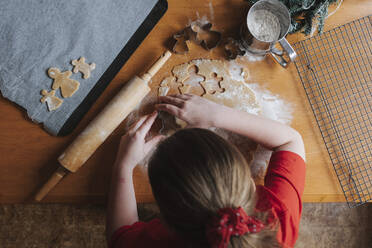 Junges Mädchen schneidet Lebkuchenteig auf einem Holztisch aus - CAVF90304