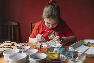 Junges Mädchen dekoriert Lebkuchen auf einem Holztisch - CAVF90310