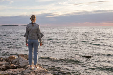 Rückenansicht einer jungen Frau, die auf dem Steinpfeiler steht und aufs Meer schaut - CAVF90328