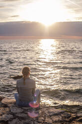 Back view of woman sitting by the sea - CAVF90329