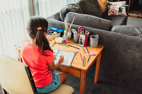 Mehrrassiges 8-jähriges Mädchen sitzt am Schreibtisch und färbt sich das Gesicht - CAVF90340