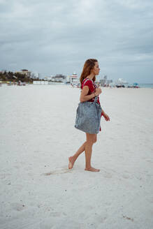 Woman with purse walking on sand at beach - MAUF03561