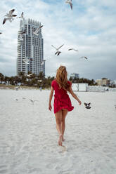 Möwe fliegt, während Frau auf Sand gegen den Himmel am Strand läuft - MAUF03570