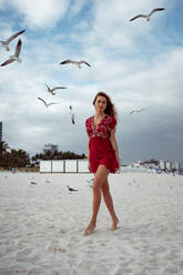 Beautiful woman standing while seagull flying against sky at beach - MAUF03571