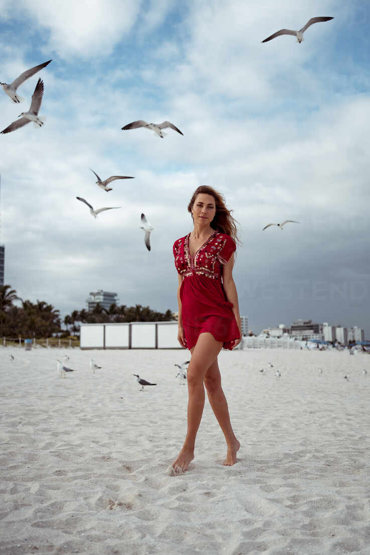 Beautiful woman standing while seagull flying against sky at beach stock  photo