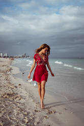 Young woman walking on shore against cloudy sky at beach - MAUF03572