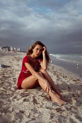 Nachdenkliche junge Frau sitzt am Strand - MAUF03576