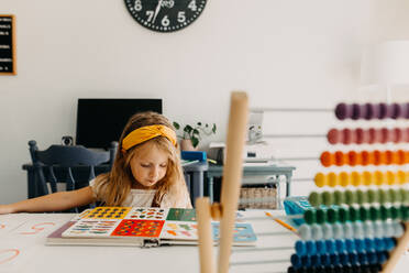 Preschool girl doing home school work at table with a book and abacus - CAVF90365