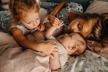 Two girls touching baby sibling and cuddling in bed together - CAVF90369