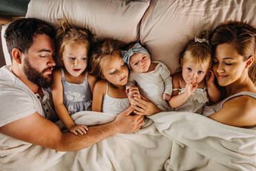 Large family laying in bed with many children and holding hands - CAVF90371