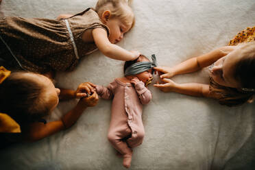 3 sisters laying in bed touching newborn baby girl with pacifier - CAVF90373