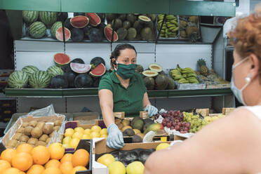 A shopkeeper with a mask attends to a customer in the greengrocer's. - CAVF90409